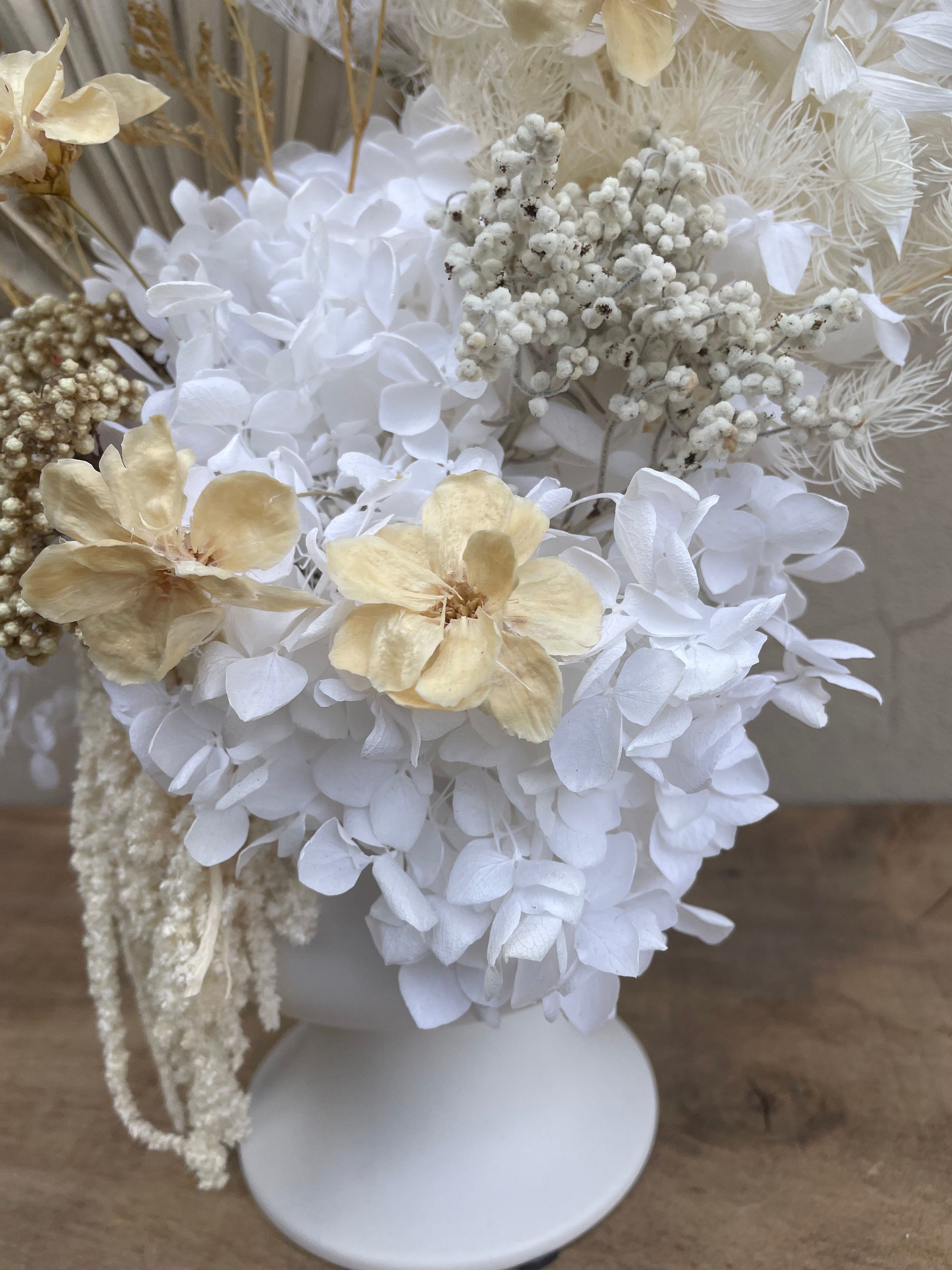 Close-up of a decorative arrangement with white and beige flowers on a wooden surface. Available for same day delivery from The Flower Boutique Perth