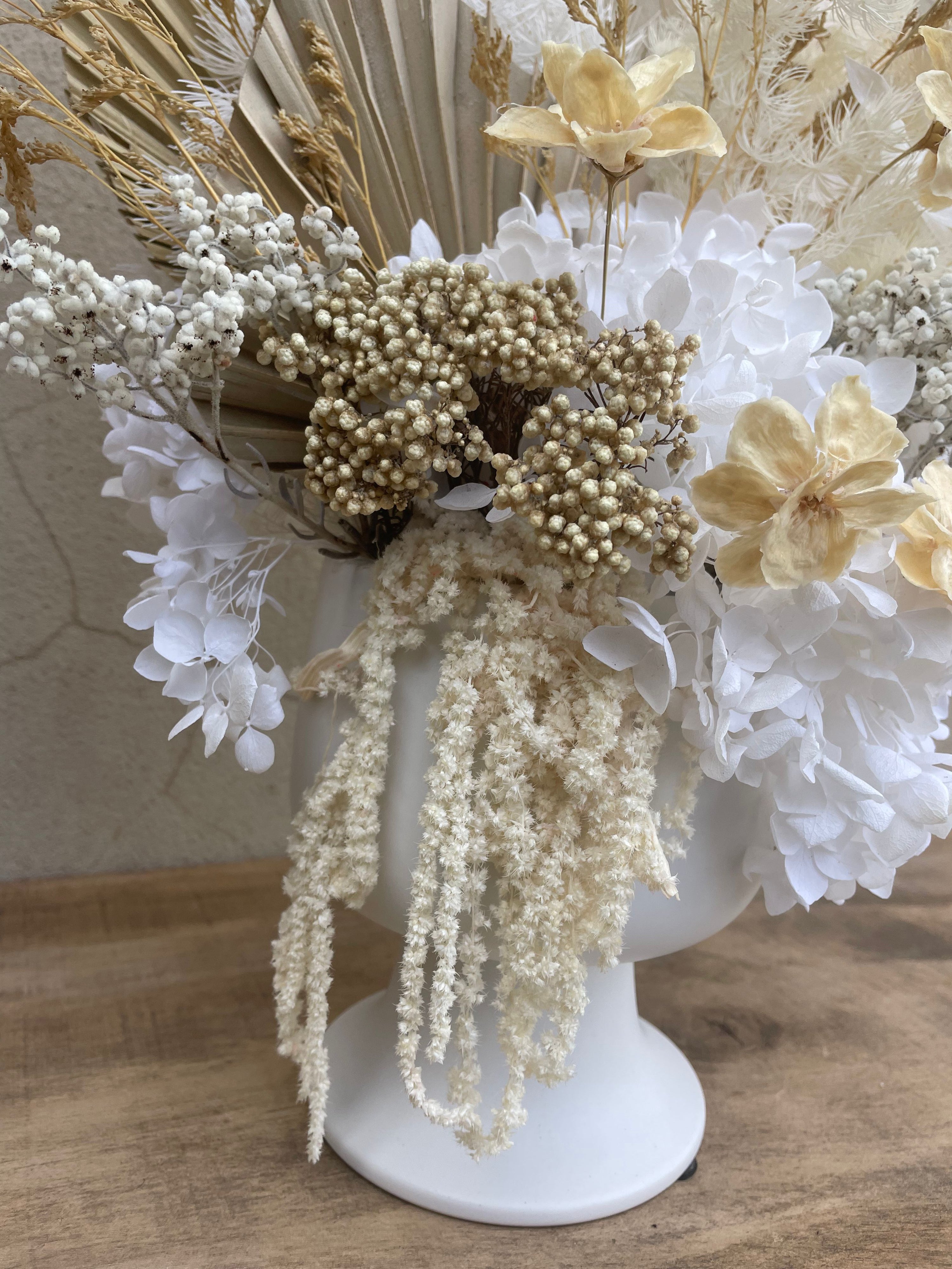 Decorative arrangement of dried flowers on a white pedestal against a neutral background