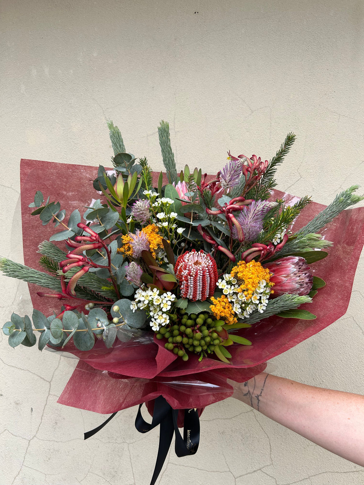 Native Instinct bouquet with pink proteas, mixed textured flowers and eucalyptus, held in burgundy wrapping