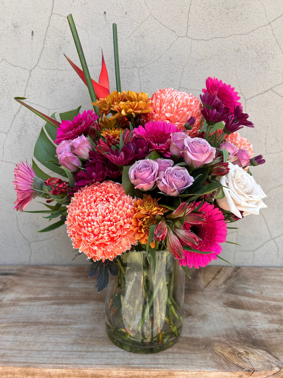 Festa Floreale vase arrangement with bright pink roses, orange flowers and green foliage in a clear glass vase