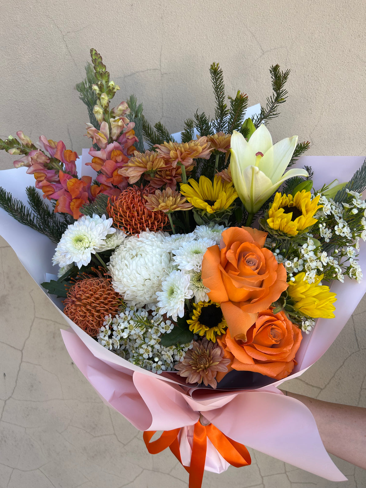 Hello Spring bouquet showing mixed orange, yellow and white flowers with fresh greenery