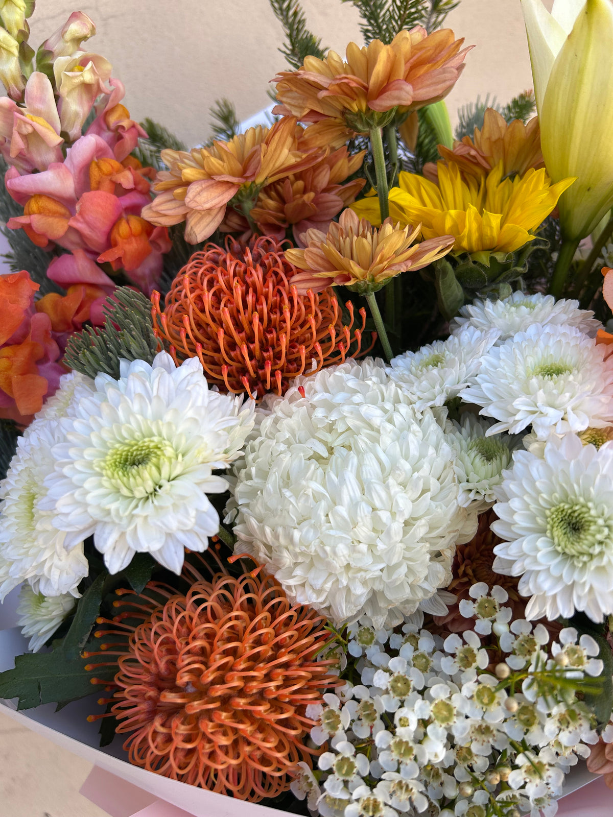 Close-up of white chrysanthemums, orange flowers and greenery in the Hello Spring bouquet avialable for delivery Perth