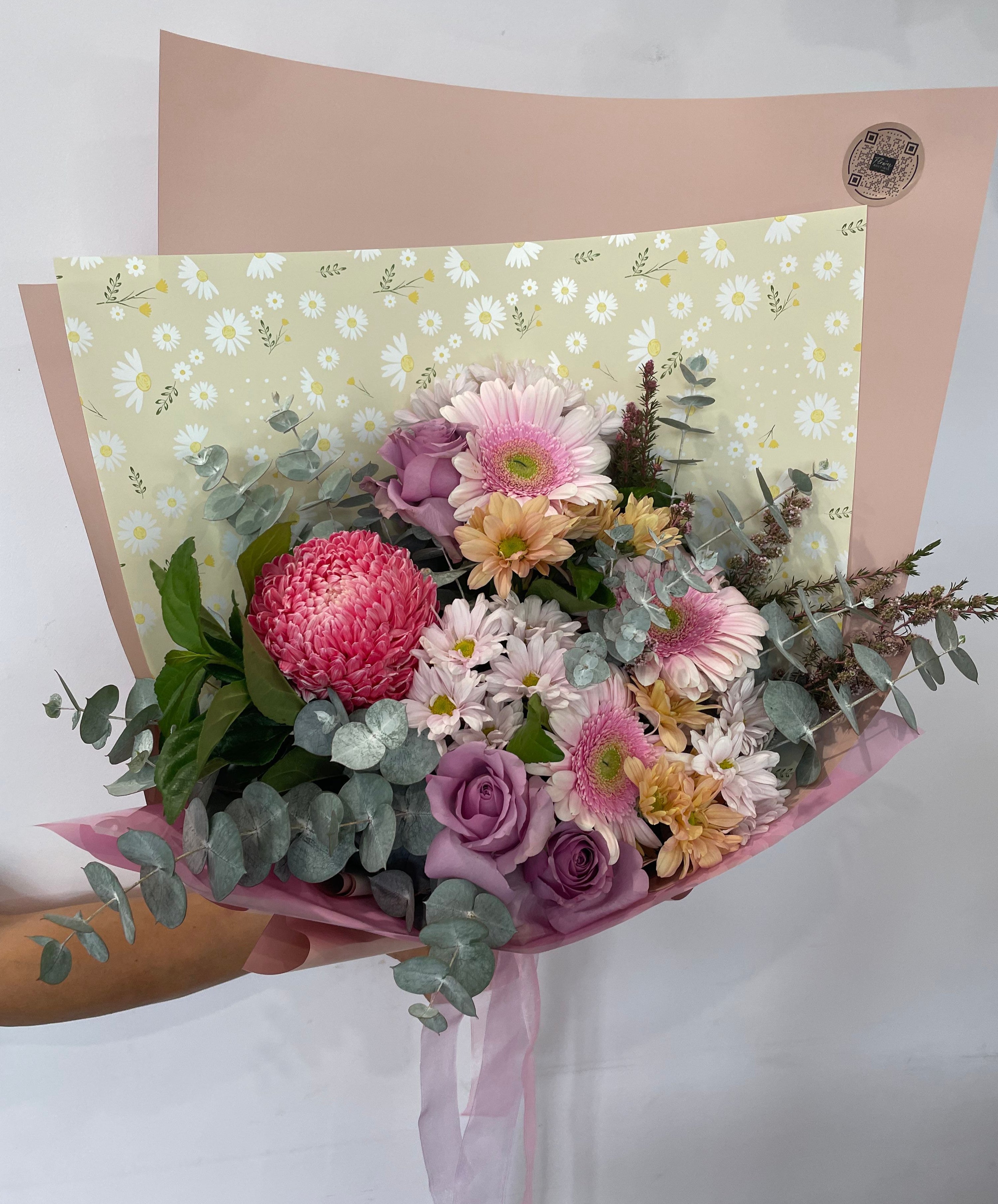 Mother’s Day flower bouquet featuring pink chrysanthemums, lavender roses, white daisies, and soft greenery wrapped in pink paper with daisy-print backing — The Flower Boutique Perth