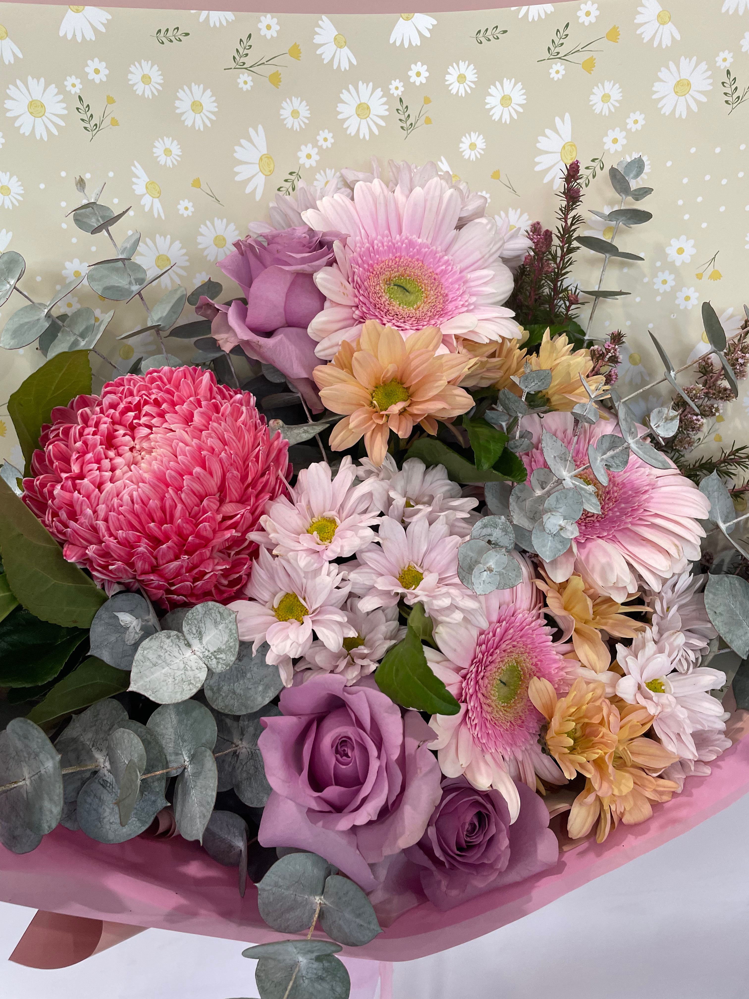 Mother’s Day flower bouquet featuring pink chrysanthemums, lavender roses, white daisies, and soft greenery wrapped in pink paper with daisy-print backing — The Flower Boutique Perth