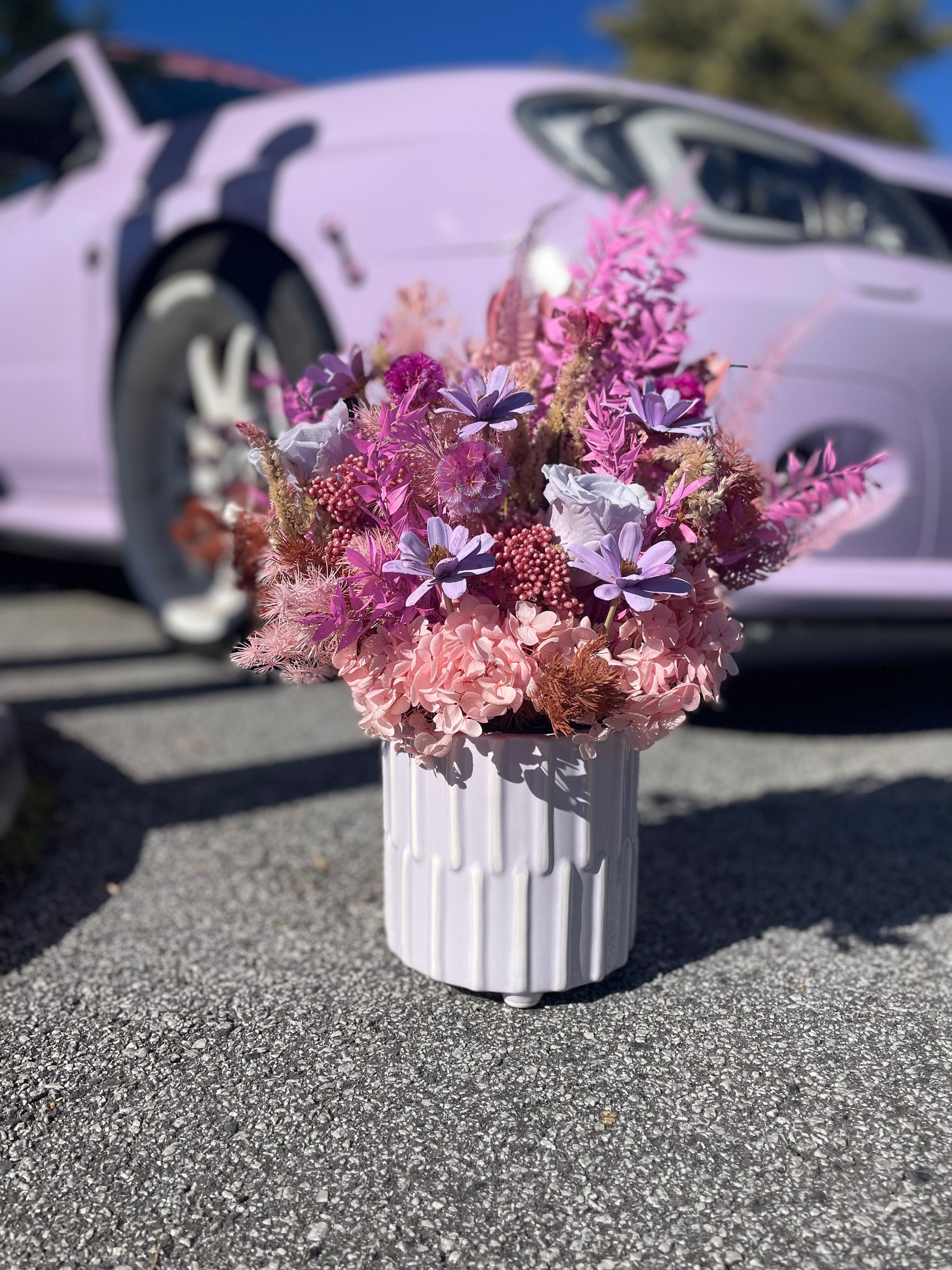 Bouquet of pink and white flowers in a white vase with a car in the background
