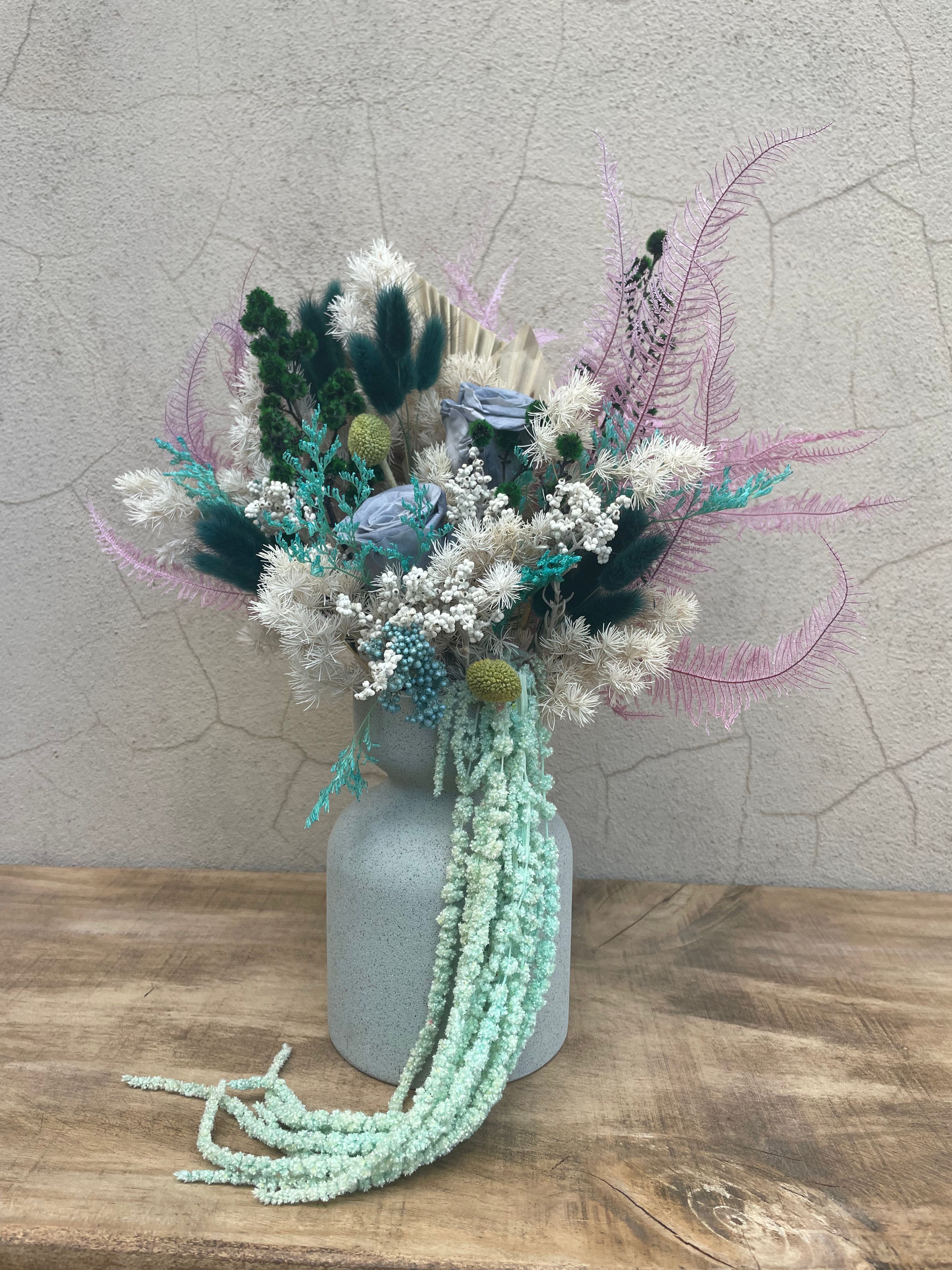 Decorative dried flower arrangement with green, white, and purple elements on a textured surface. order today for same day delivery accross Perth from The Flower Boutique Joondalups best florist