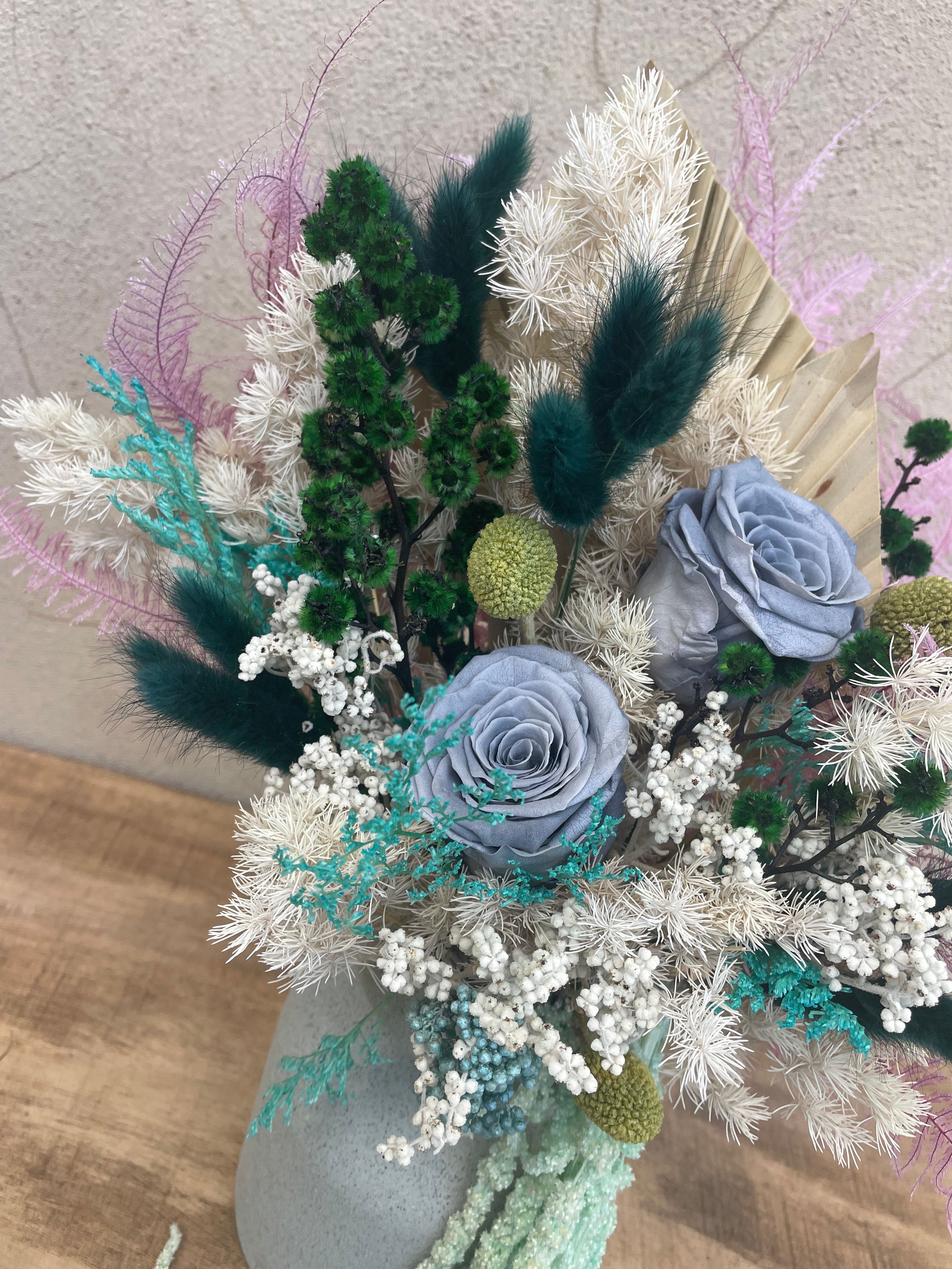 Decorative dried flower arrangement with green, white, and purple elements on a textured surface. order today for same day delivery accross Perth from The Flower Boutique Joondalups best florist