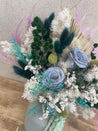 Decorative dried flower arrangement with green, white, and purple elements on a textured surface. order today for same day delivery accross Perth from The Flower Boutique Joondalups best florist