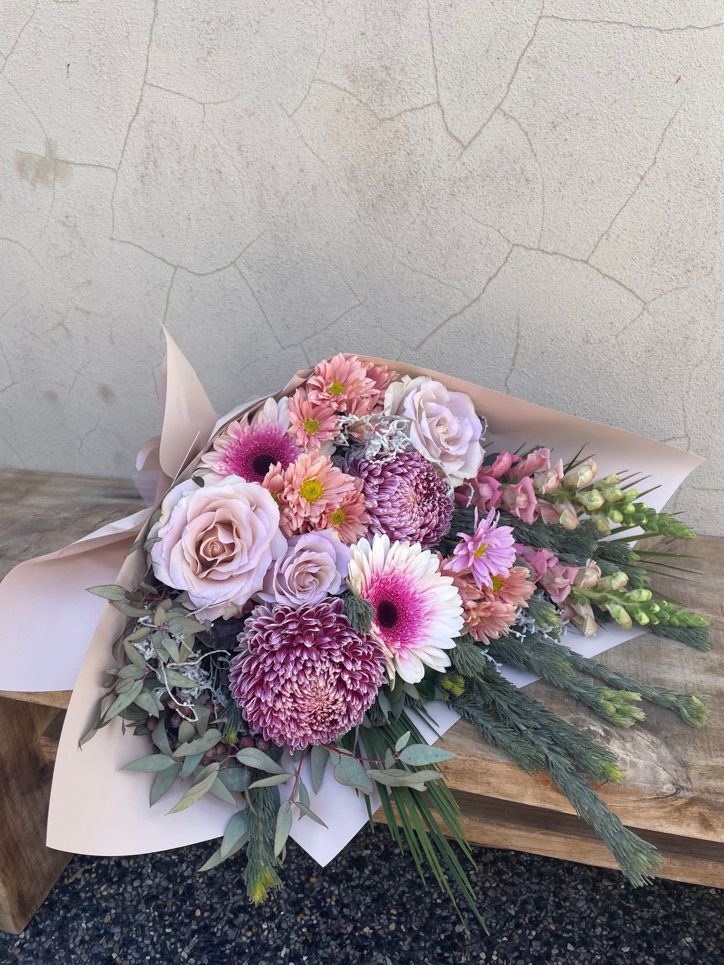 Bouquet of pastel pink tones, fresh flowers on a wooden board with a concrete floor background available for same day delivery accross perth
