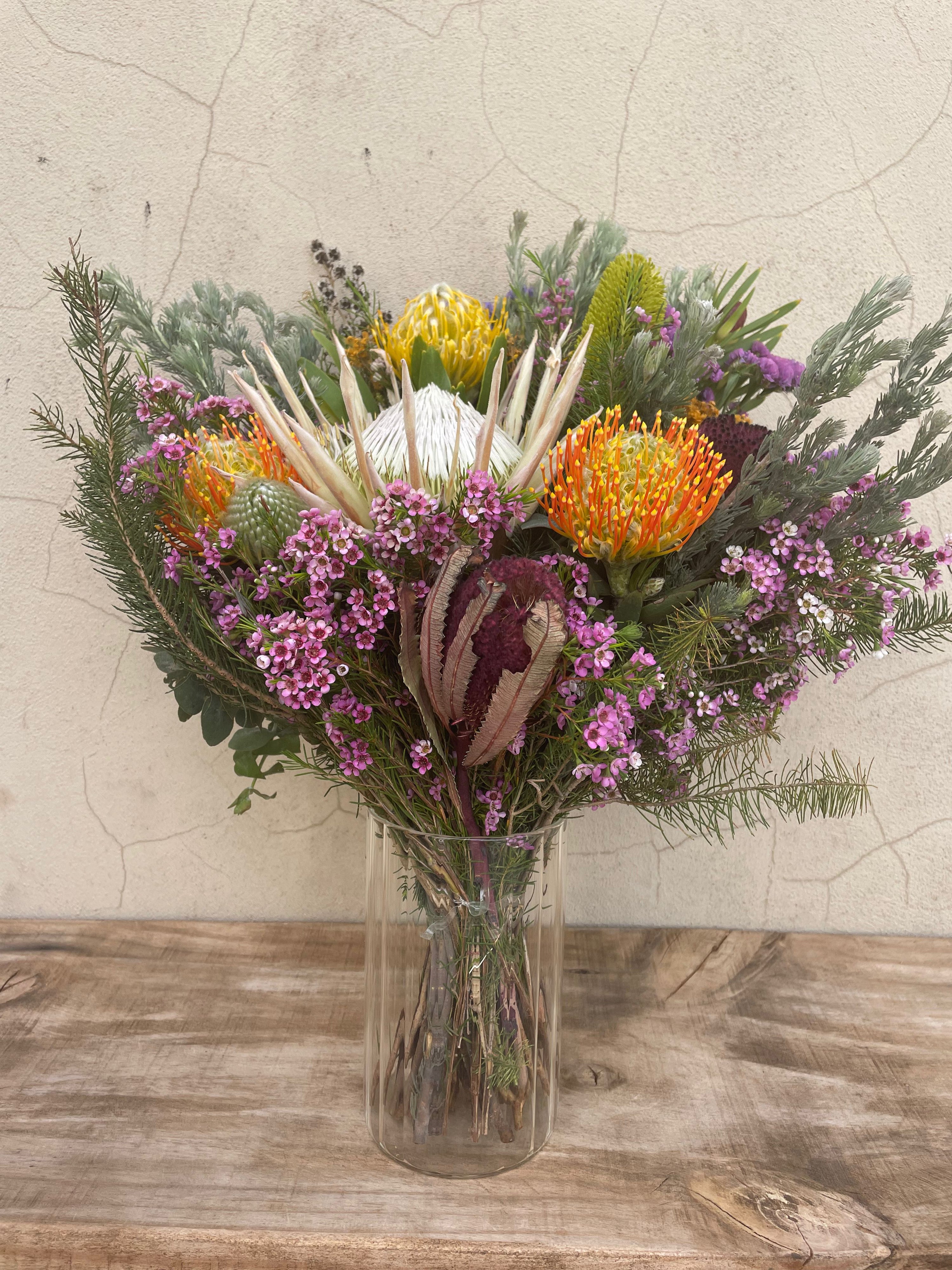 Native flower vase arrangement featuring a white King Protea, pincushions, wax flower and native foliage in a clear glass vase. Hand-crafted by The Flower Boutique Perth.