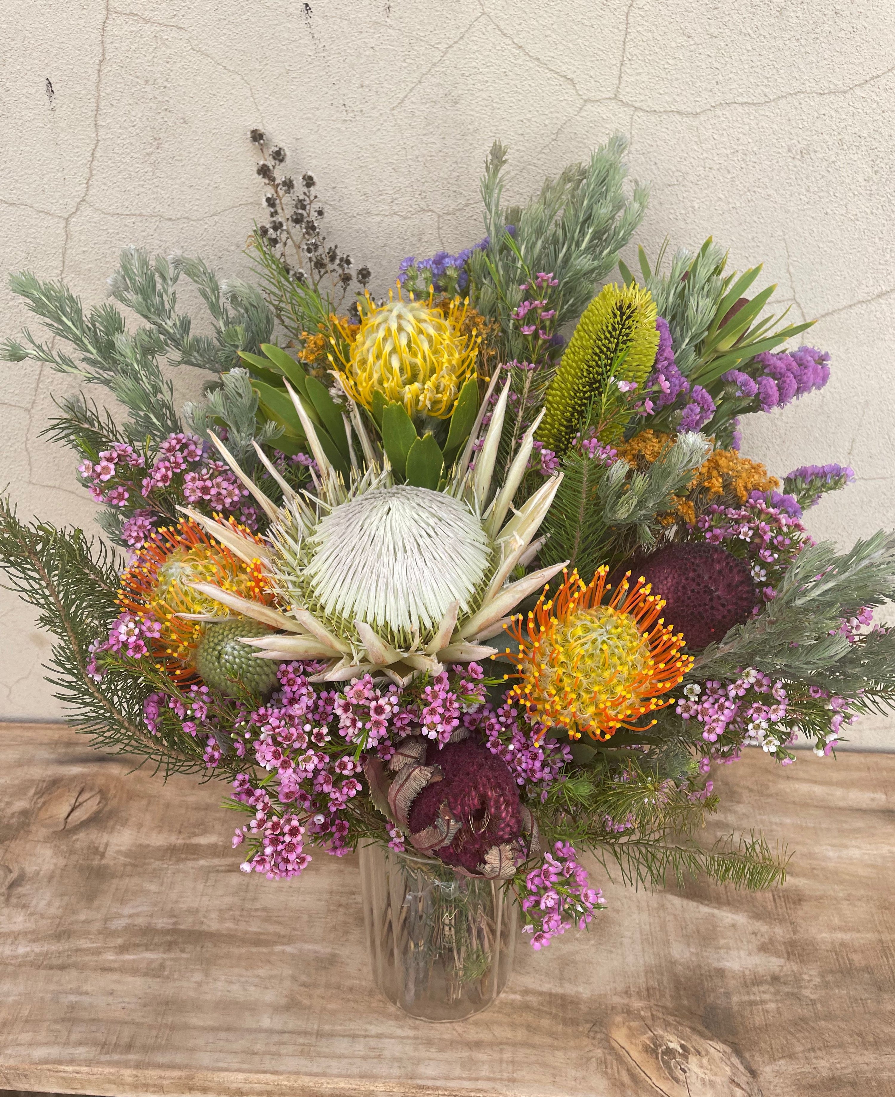 Native flower vase arrangement featuring a white King Protea, pincushions, wax flower and native foliage in a clear glass vase. Hand-crafted by The Flower Boutique Perth.