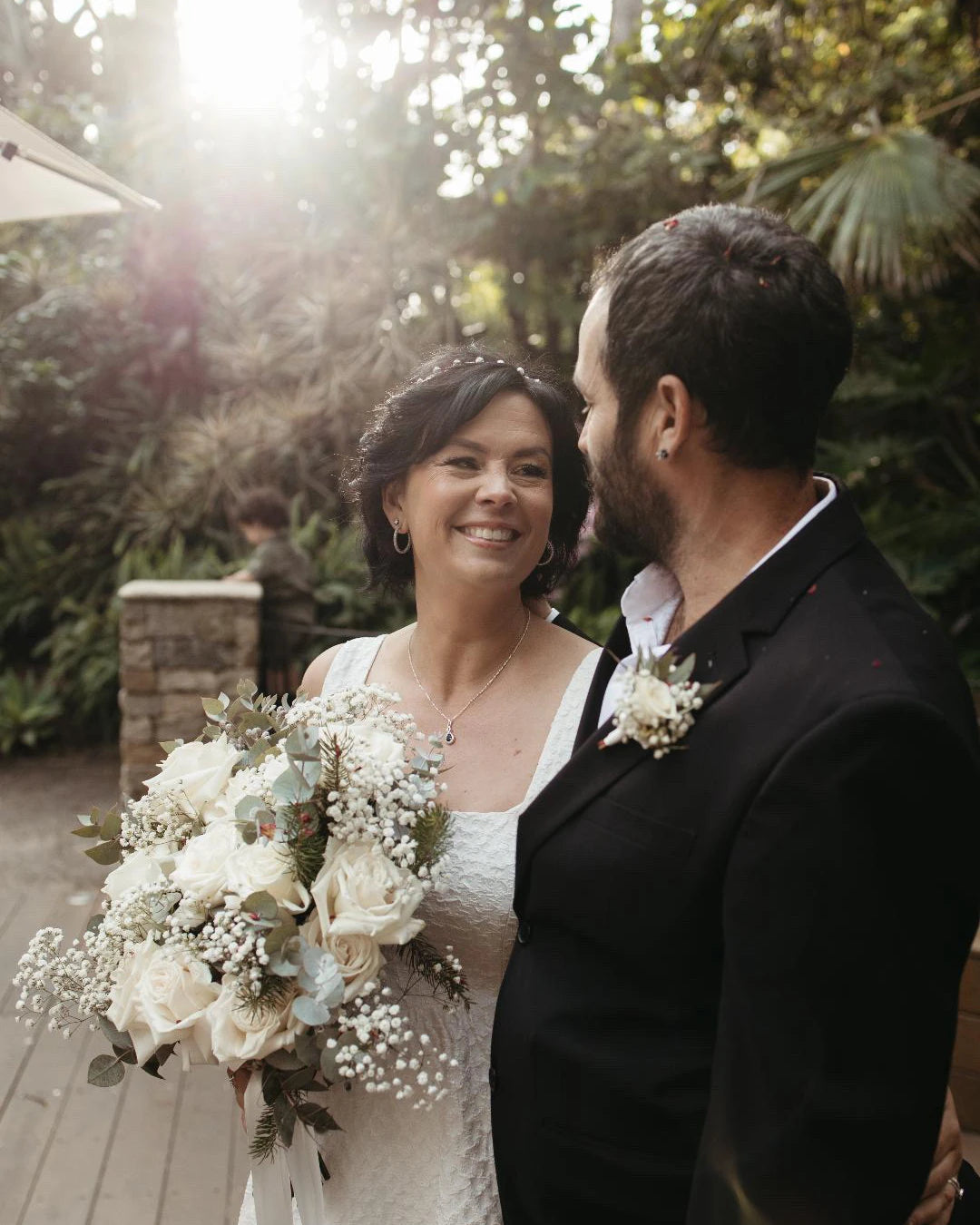 Wedding couple standing smiling with a beautiiful bouquet of flowers. At The Flower Boutique our expert florist Riana Bertolami does strunning flowers for all kinds of events like weddings, funerals or corporate gatherings. Get in touch with us now located in Ashby, Perth 6065