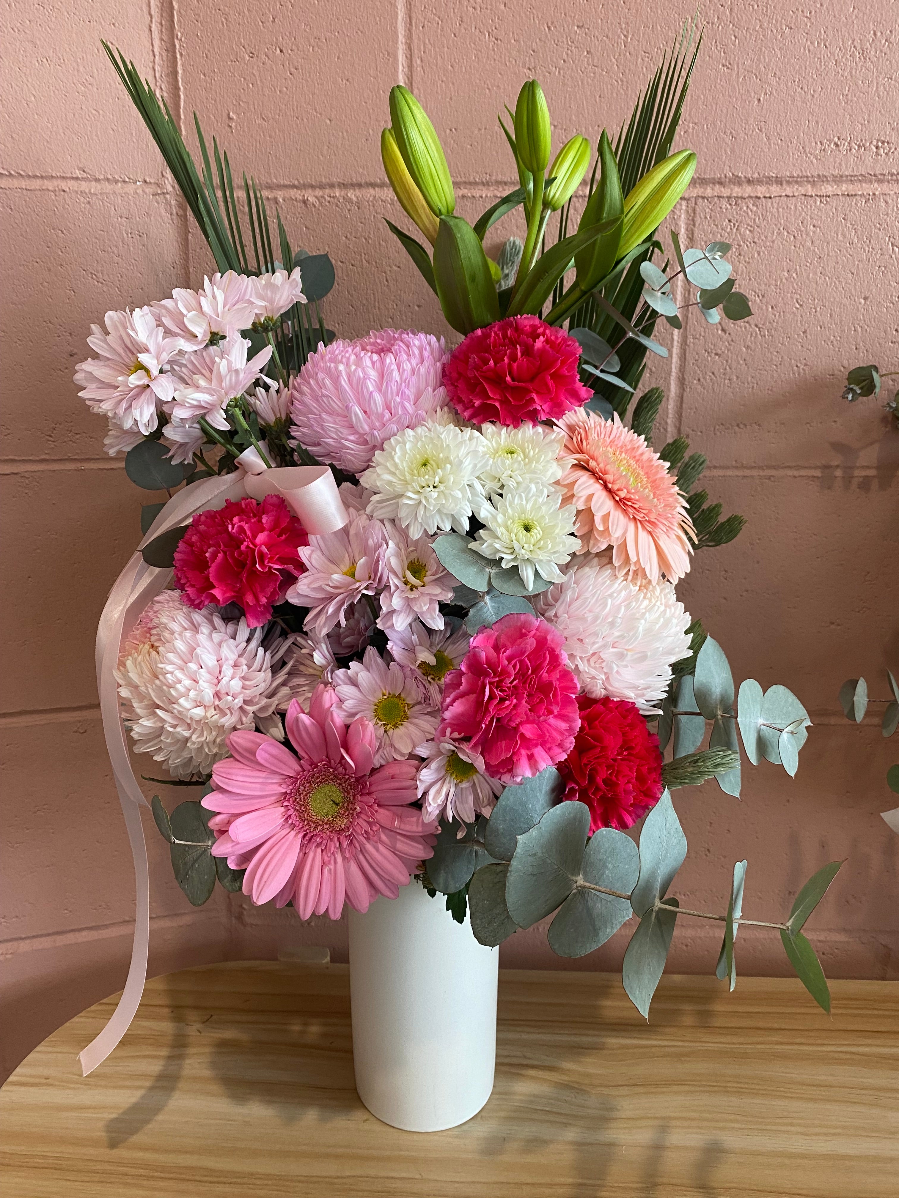 A vase arrangement bouquet of flowers with pink, red, and white colors against a wooden background available for online order and same day flower delivery in perth metro.