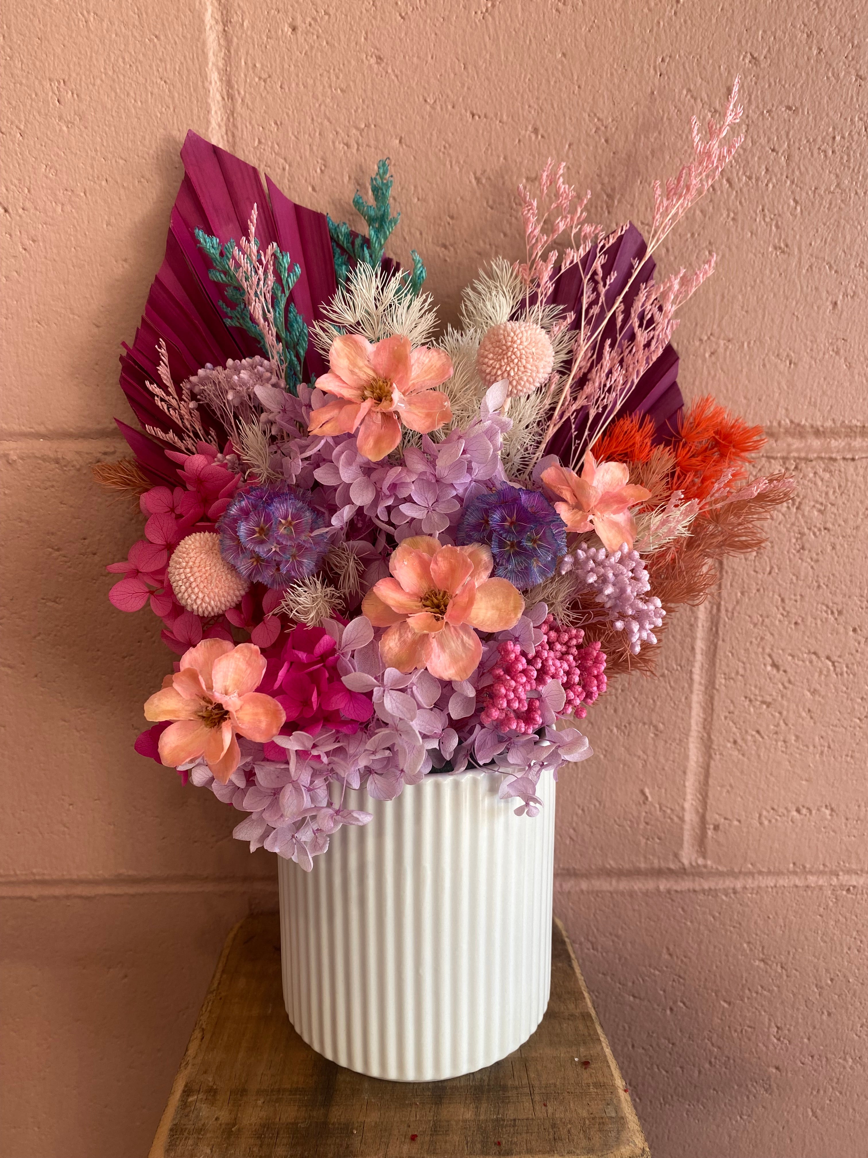 Tutti Fruiti dried flower arrangement by The Flower Boutique – preserved pink, purple, coral and magenta blooms in a white ribbed ceramic vase