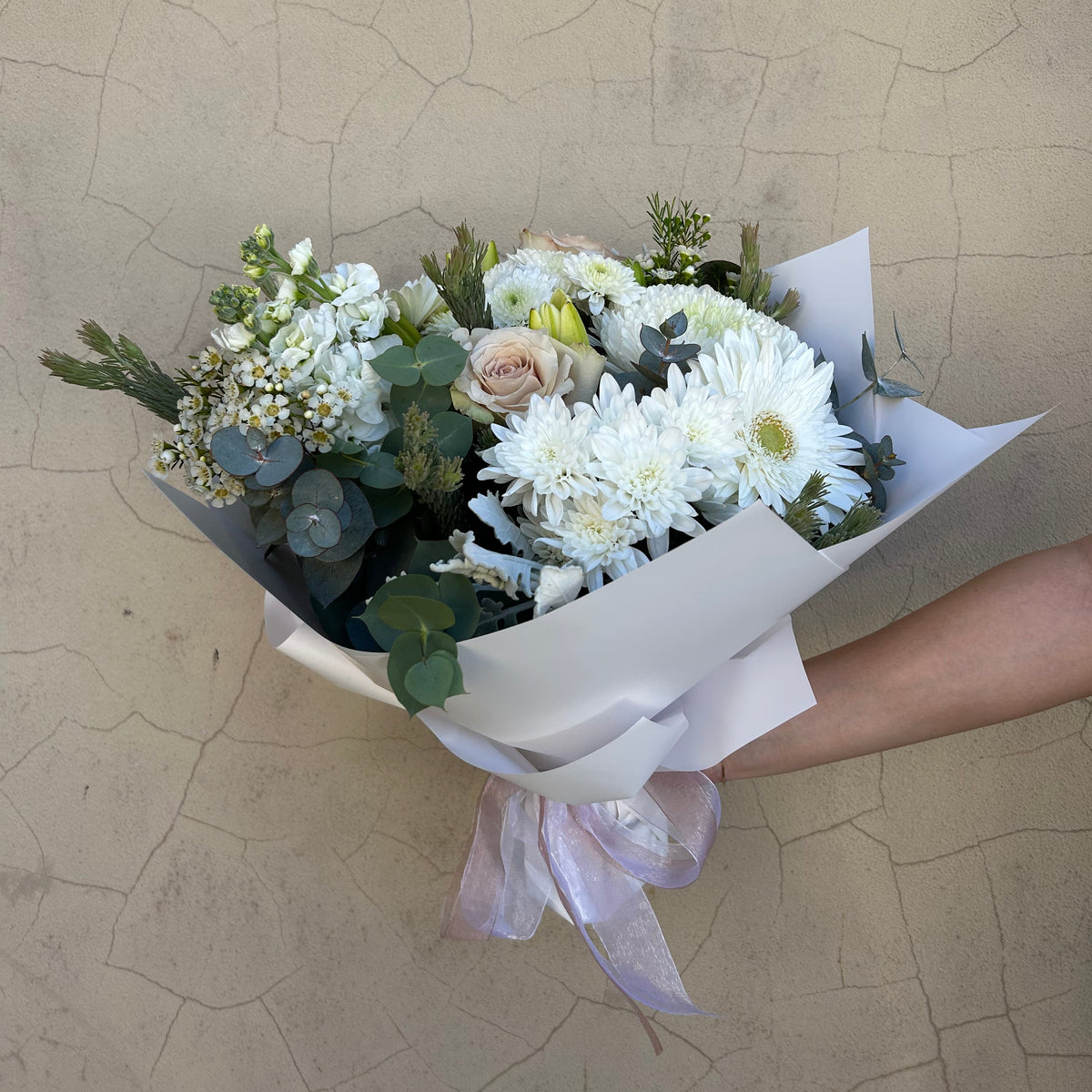 Simplicity white and neutral bouquet with green foliage, held in white wrapping with a pale ribbon