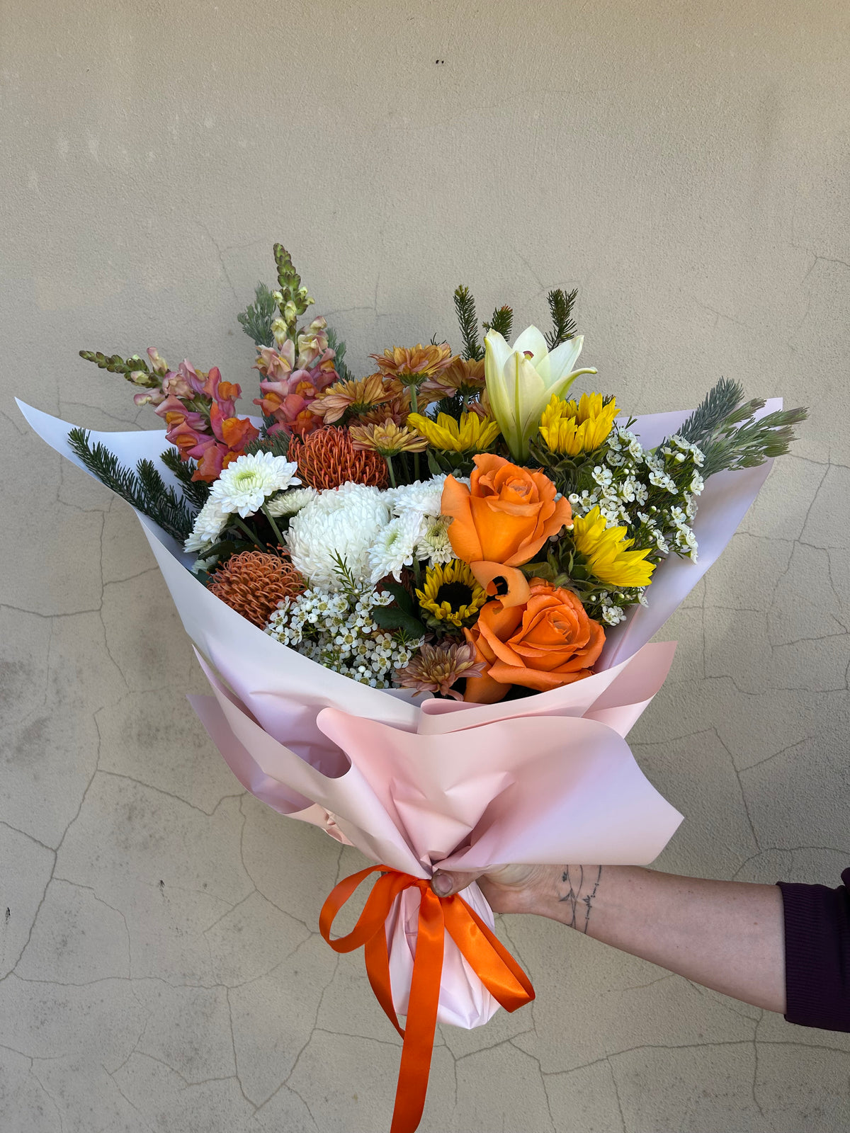Hello Spring bouquet with orange roses, yellow and white flowers, wrapped in pink paper with an orange ribbon