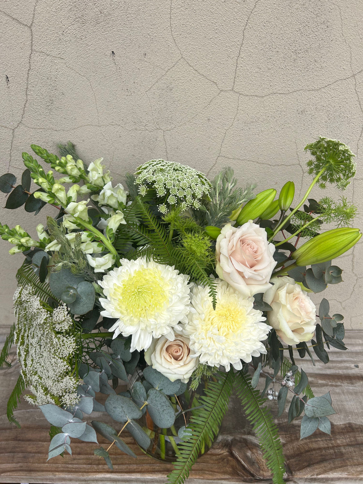 Close-up of cream roses, white chrysanthemums, lily buds and green foliage in the Grande sympathy vase